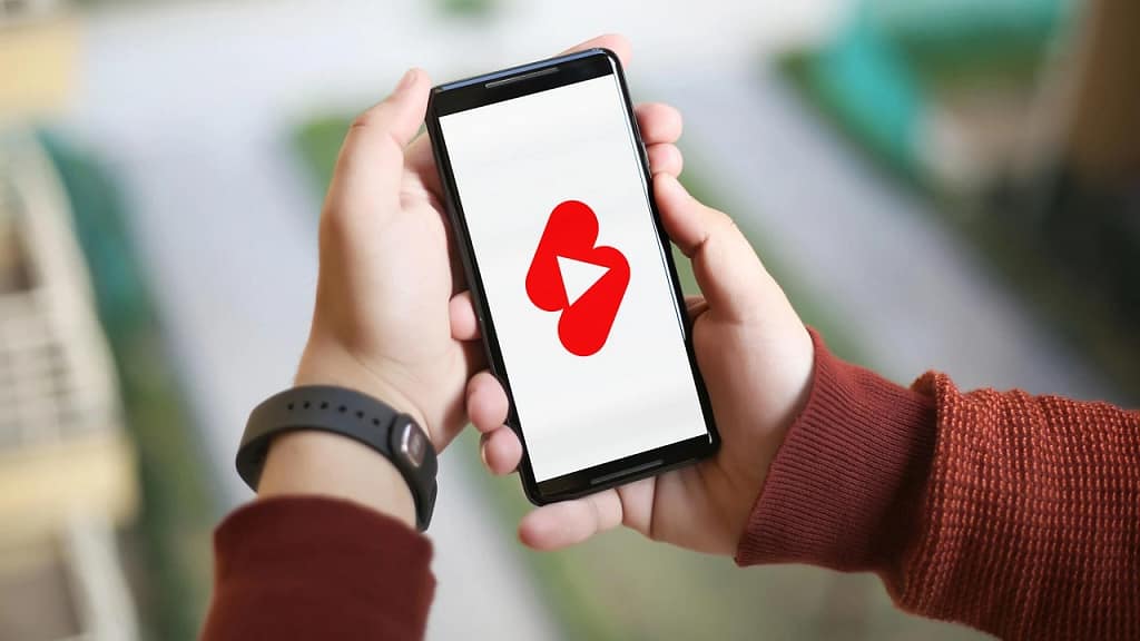 Person holding a smartphone displaying a red video display icon on the screen