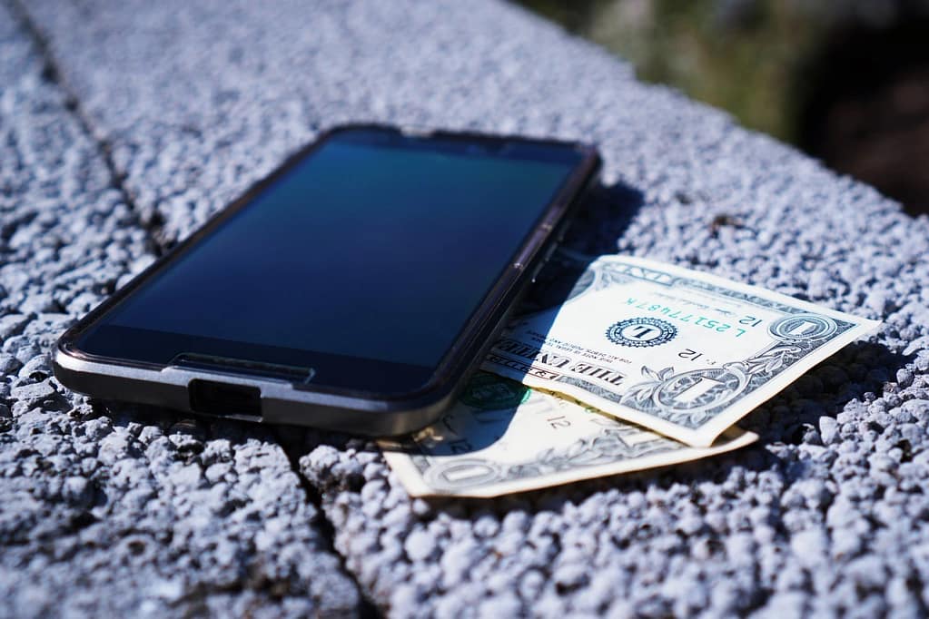A black smartphone resting on top of cash notes representing budget phone savings