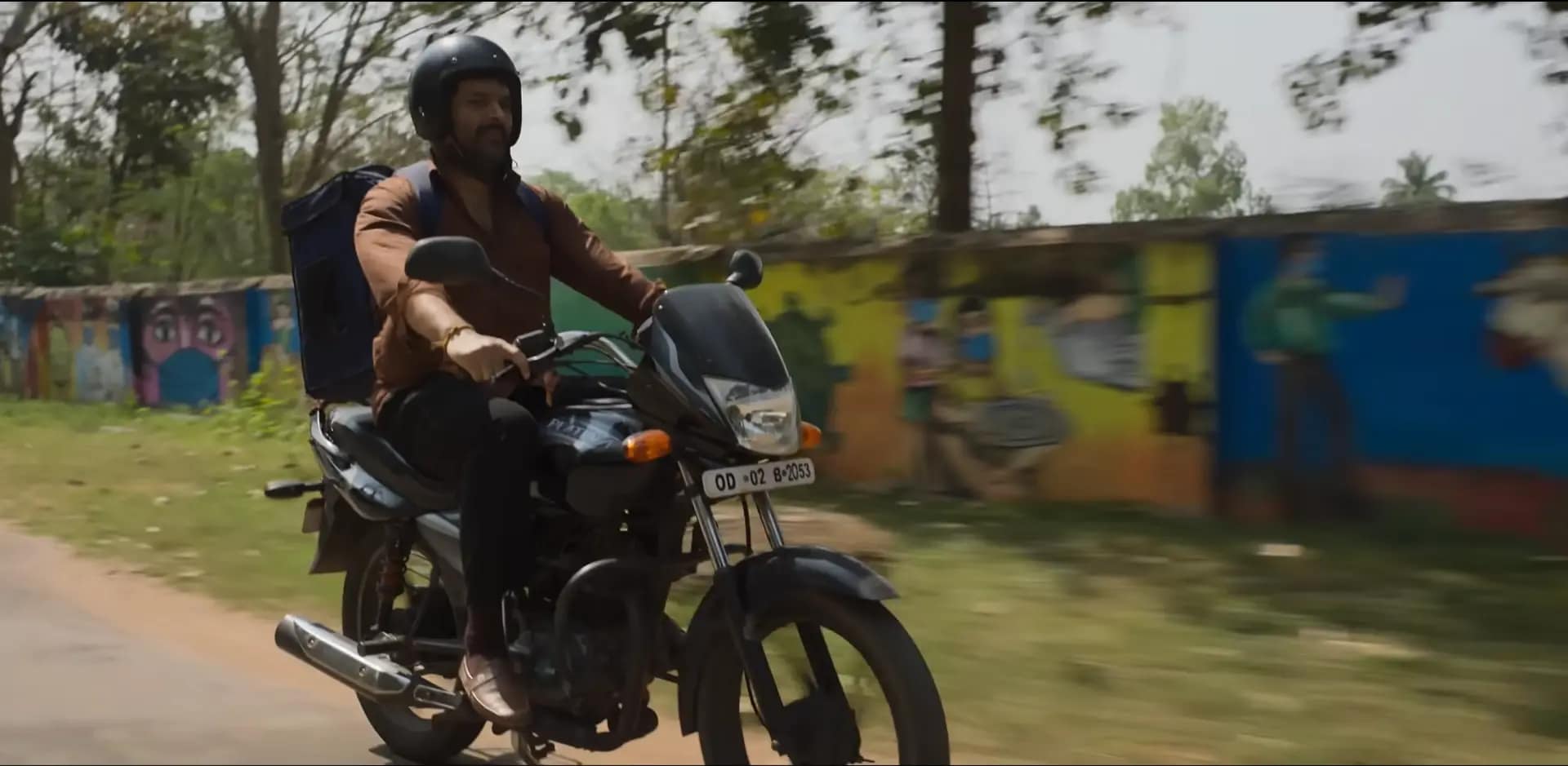 Kapil Sharma as Manas Mahto riding a motorcycle with a food delivery bag in Zwigato (2022).