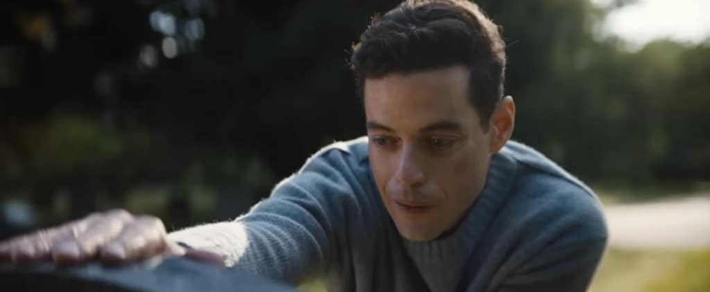 A close up of Charlie Heller’s (Rami Malek) emotional reaction while touching Sarah Heller’s tombstone, highlighting the theme of personal loss in The Amateur (2025).
