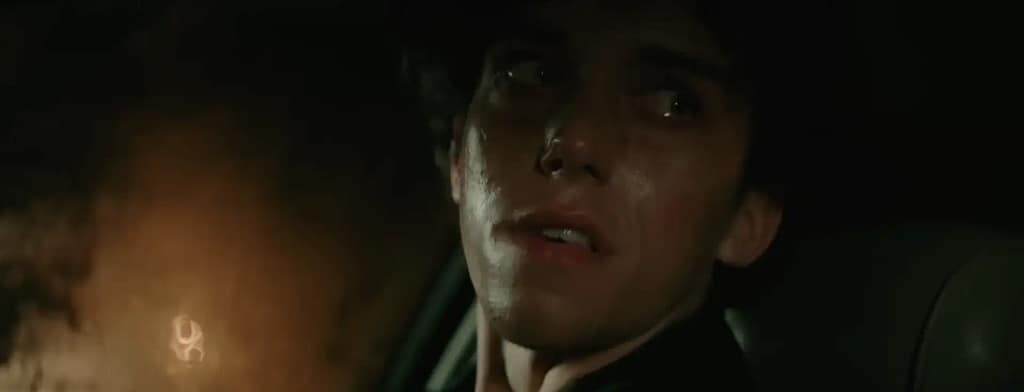 Close-up shot of Sean Thomas Reid as Harry Osborn displaying intense emotional pain and isolation inside a dark car scene.