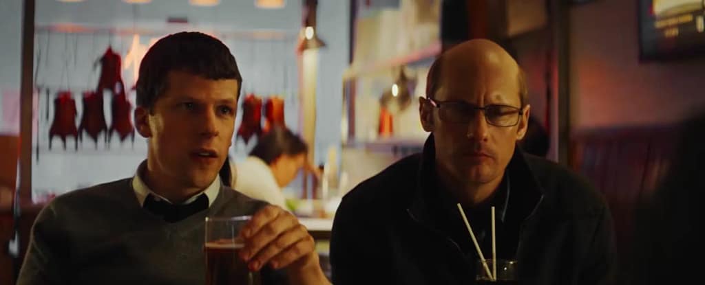 Jesse Eisenberg as Vincent Zaleski and Alexander Skarsgård as Anton Zaleski sitting together in a restaurant in The Hummingbird Project. Image credit: The Hummingbird Project (2018) film still - via Rotten Tomatoes Trailers/YouTube.