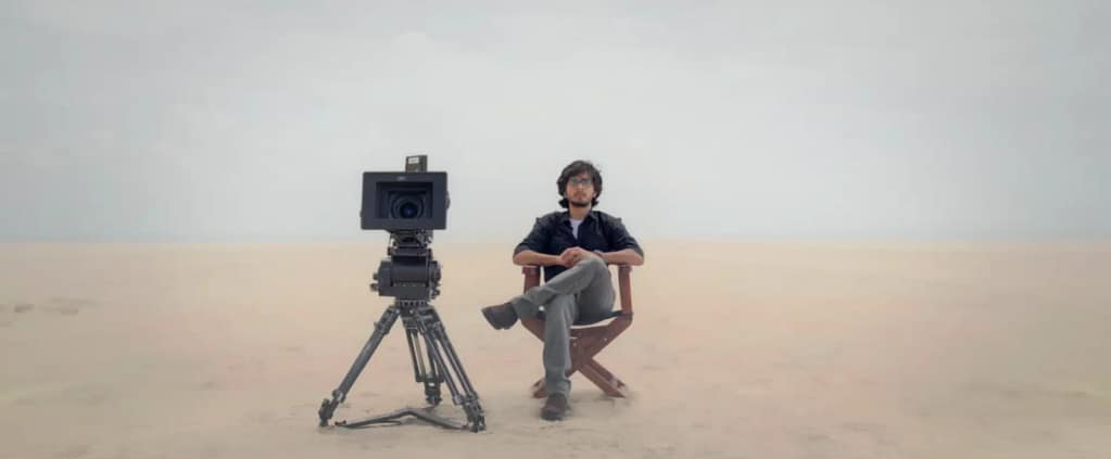Naslen sitting in a director’s chair next to a cinema camera on a vast desert set in Mollywood Times. Image credit: Mollywood Times (2026) film still - via Sony Music Malayalam/YouTube.