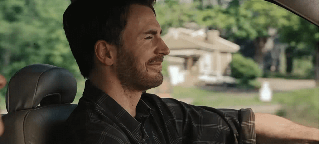 Chris Evans smiling while driving a car as John Pitts in Celine Song’s Materialists (2025).