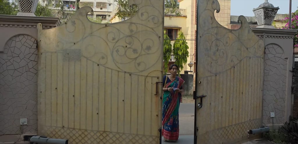Shahana Goswami as Pratima looking anxiously at the large iron gate of a wealthy house in Zwigato (2022).