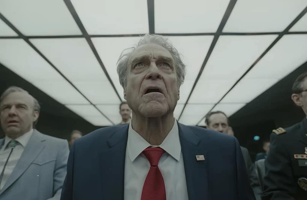 Tom Cruise as Digger Rockwell and John Goodman as President Compson looking upwards in shock in a brightly lit room. Image credit: Digger (2026) film still - via Warner Bros./IMAX/YouTube.