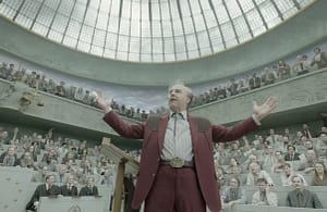 Tom Cruise as Digger Rockwell standing with arms open in a curved courtroom filled with onlookers. Image credit: Digger (2026) film still - via Warner Bros./IMAX/YouTube.